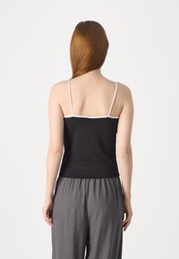 Svart tanktop med tynne hvite stropper, som har en tettsittende design og en glatt tekstur, kombinert med løse grå bukser.