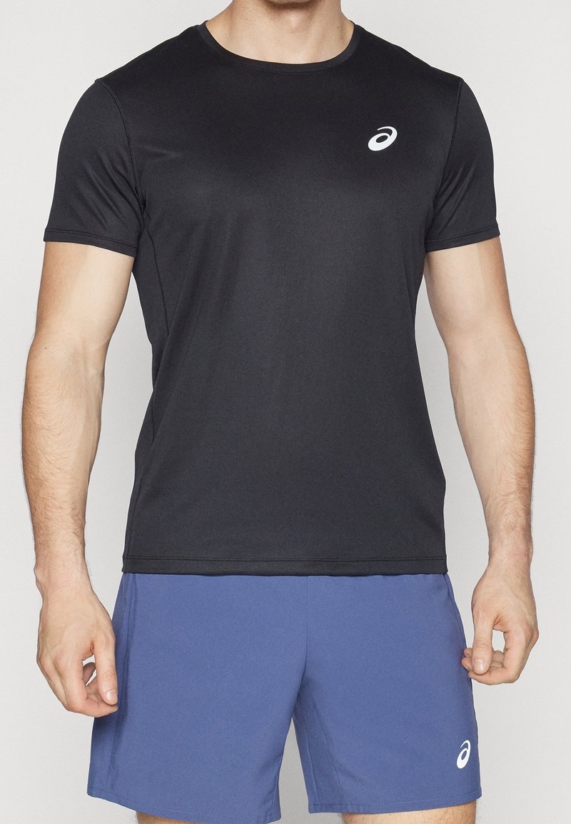 Svart atletisk t-shirt med korta ärmar, tillverkad av ett slätt tyg, med en liten vit logotyp på vänster bröstområde.