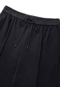 Czarne dresy z elastycznym pasem, regulowanym sznurkiem i bocznymi kieszeniami, charakteryzujące się gładkim, teksturowanym materiałem oraz plisowanym wzorem.