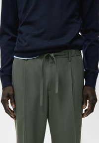 Suéter de punto azul marino con cuello redondo, combinado con pantalones verde oliva con cinturón de lazo y textura suave, mostrando detalles frontales y de la cintura.