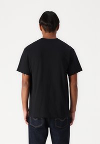 Sort bomulds T-shirt med korte ærmer, rund hals og en afslappet pasform. Modellen har blå denim jeans på, som har minimal detaljering.