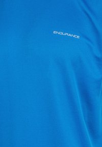 Kirkkaan sininen urheilupaita, joka on valmistettu sileästä kankaasta. Edessä valkoinen "ENDURANCE"-logo, istuva leikkaus ja lyhyet hihat.