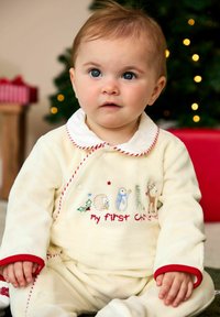 Ensemble de pyjama en polaire de couleur crème avec des accents rouges. Présente des broderies d'animaux de la forêt et le texte « mon premier Noël ». Texture douce et confortable.