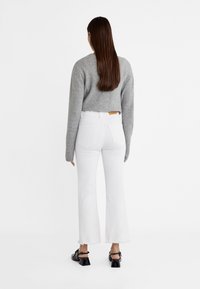 Suéter gris recortado con cuello redondo, combinado con jeans blancos acampanados con dobladillo deshilachado y sandalias planas negras.