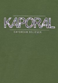 Camiseta verde oliva con un audaz estampado texturizado de "KAPORAL" y "DAYDREAM BELIEVER" en blanco y acentos multicolores.