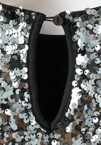 Musta vaate, jossa on V-pääntie ja napillinen suljin. Päällystetty monivärisillä paljeteilla, jotka heijastavat hopean, harmaan ja ruskean sävyjä.