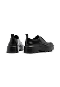 Scarpe in pelle nera con punta rotonda, suola in gomma resistente e cuciture a contrasto. Presentano un tacco leggero e un passante sul retro.