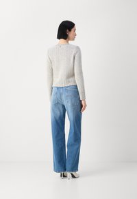 Grijze herringbone gebreide trui met lange mouwen, cropped stijl, gecombineerd met hooggesneden blauwe denim jeans en witte hakken. Achteraanzicht.