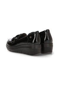 Zapatos de charol negros con puntera redonda, suela acolchada y tacón bajo tipo cuña. Presenta un detalle de correa en el empeine.
