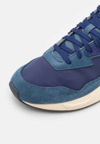 Baskets bleu marine avec une combinaison de cuir lisse et de suède texturé. Dotées d'une semelle rembourrée et de lacets bleus, accentués de détails bleu clair.