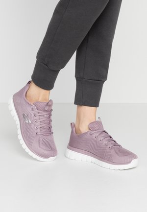 Zapatillas deportivas moradas con parte superior de malla transpirable, cierre de cordones y suela blanca acolchada, con textura en zigzag y detalle de logo.