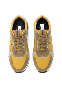Scarpe da ginnastica gialle e beige con una tomaia in sintetico liscio, dettagli in suede e lacci rotondi. Presentano una suola ammortizzata e un logo sulla soletta.