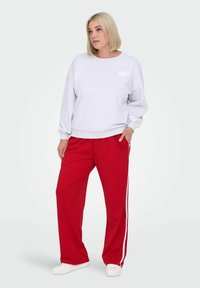 Svetlo siva trenerka s okruglim izrezom i belim natpisom "PARIS", u kombinaciji sa crvenim pantalonama sa belim bočnim prugama. Oba komada imaju opušteni kroj.