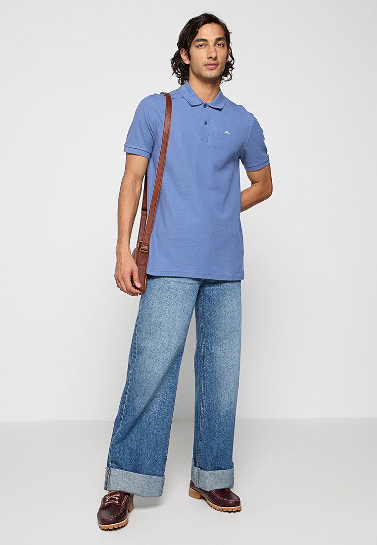 Ljusblå polo med klassisk krage, tillsammans med vida ljusa denimjeans och bruna läderskor. Brun axelväska ingår.