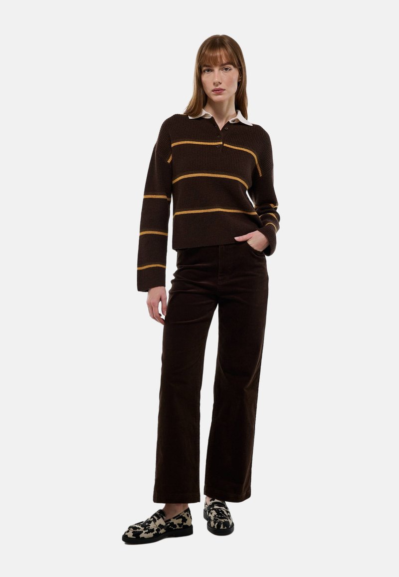 Pull en laine marron avec des rayures jaunes et un col blanc, associé à un pantalon large en velours côtelé marron et des mocassins à motifs.