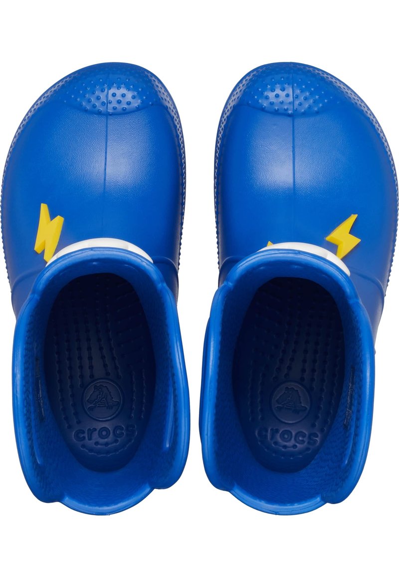 Zuecos de goma azules con acentos de relámpago amarillos y plantillas texturizadas. Superficie suave con punta redondeada y tacón elevado, diseñados para la comodidad.