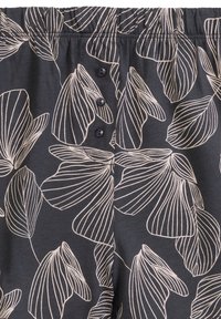 Ciemne materiałowe spodnie piżamowe z białym wzorem liści, elastycznym paskiem w talii oraz trzema guzikami w pasie. Miękki materiał o gładkiej fakturze.