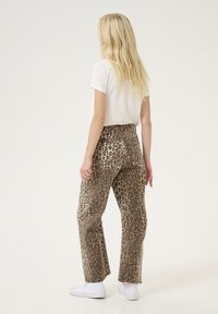 Pantalons à motif léopard avec une coupe décontractée, dotés d'une taille haute et de poches arrière, associés à un t-shirt blanc et des baskets blanches.