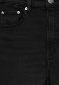 Gros plan sur un jean en denim noir montrant la poche avant, la petite poche à monnaie avec deux rivets, la passants de ceinture et le bouton en métal sur la ceinture.