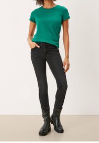 Camiseta de algodón verde con mangas enrolladas, combinada con jeans skinny negros y botas negras hasta el tobillo. Texturas suaves y diseño ajustado.