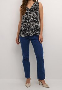 Top sin mangas con escote en V en patrón blanco y negro. Combinado con jeans azules y mules de tacón beige. Tejido suave con un corte relajado.