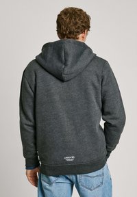 Sudadera gris oscuro con una capucha grande, tela texturizada, puños acanalados y un pequeño logo en el dobladillo. Presenta un corte relajado y un diseño casual.
