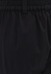 Černé šortky vyrobené z lehkého materiálu, s elastickým pasem, hladkou texturou a uvolněným střihem. Bez viditelných vzorů nebo akcentů.