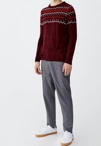 Suéter de punto burdeos con un yugo estampado en rojo, blanco y negro; pantalones grises; zapatillas blancas con suelas marrones; diseño minimalista.