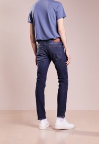 Mörkblå denimjeans med slim fit, med bakfickor som har en distinkt logotyp, kombinerade med en avslappnad blå t-shirt och vita sneakers.