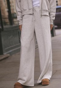 Hellgraue weite Sweatpants mit strukturierter Oberfläche, ausgestattet mit einem elastischen Bund und Kordelzug. Kombiniert mit tanfarbenen Plateauschuhen zum Hineinschlüpfen.
