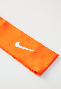 Kollane Nike peapael, mis on valmistatud siledast kangast, valge swooshi logoga. Ese on korrektselt volditud ja sellel on puhas viimistlus.