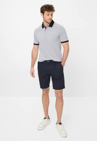 Polo a maniche corte da uomo in blu chiaro con motivo geometrico bianco, abbinato a pantaloni shorts blu navy, dotati di due tasche laterali e sneakers bianche.