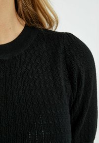 Pull en tricot noir avec un motif texturé, un col côtelé et des manches légèrement bouffantes. Orienté vers le détail avec un design décontracté.