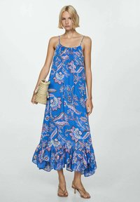 Blaues florales Maxikleid mit dünnen Trägern, rüschensaum und lässiger Passform. Mit rosa und weißen Mustern. Accessoire: geflochtene Korbtasche.