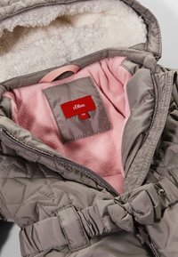 Šedá prošívaná bunda s hřejivou růžovou fleecovou podšívkou a látkovou náplastí. Obsahuje dekorativní pásek a zapínání na zip.