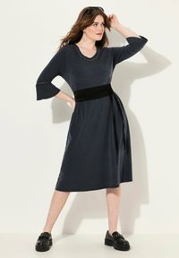 Czarna sukienka w kolorze ciemnogranatowym z rękawami trzyczwartowymi w kształcie dzwonu, okrągłym dekoltem ozdobionym ćwiekami oraz czarnym paskiem materiałowym podkreślającym talię.