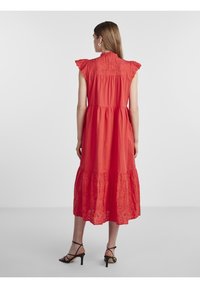 Robe rouge longueur cheville avec des manches à volants, design à plusieurs niveaux et accents en dentelle brodée sur l'ourlet, dotée d'une fermeture par bouton au dos.
