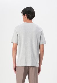 Tricou din bumbac gri, cu mâneci scurte, gât rotund și croială lejeră. Textură netedă și design simplu, văzut din spate.