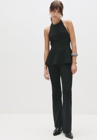 Sort peplum top kombineret med tætsiddende sorte bukser. Glat stof, halterneck-design og flagrende ankellang kant. Sølvfajance som accent.