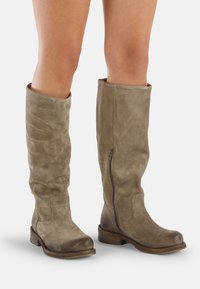 Botas de ante taupe hasta la rodilla, con una textura ligeramente desgastada, punta redondeada y cremallera lateral, que presentan un tacón bajo y apilado.