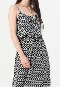 Robe à motifs noir et blanc avec une coupe décontractée, des bretelles spaghetti et un détail de taille froncée, présentant un design géométrique.