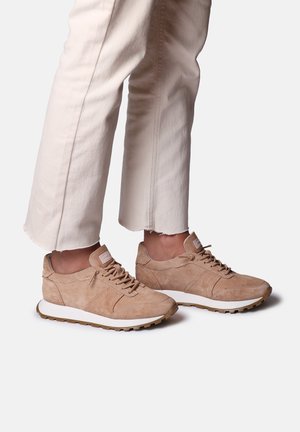 Beżowe zamszowe sneakersy z sznurowaniem, biała podeszwa środkowa i teksturowana guma na zewnątrz. Połączone z jasnymi, krótkimi dżinsami.