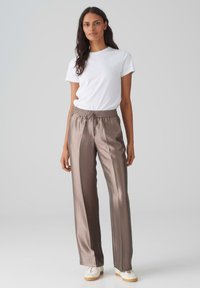 Lichtbruine satijnen broek met een elastische tailleband en trekkoord, gecombineerd met een simpel wit T-shirt en witte sneakers.