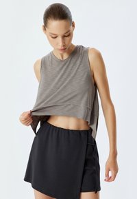 Top corto senza maniche grigio chiaro con scollatura arrotondata, caratterizzato da una superficie texturizzata; abbinato a un pantaloncino nero a vita alta con coulisse.