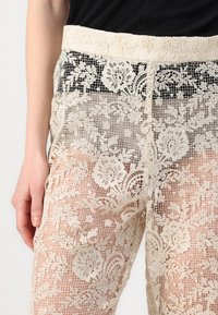 Pantalons en dentelle avec un design transparent et motif floral en ivoire, une taille élastique et une finition légère et texturée.