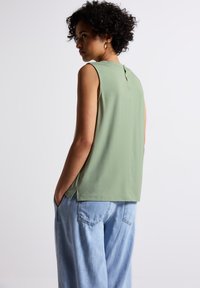 Sleeveless top in soft green fabric with a keyhole detail at the back, paired with loose blue denim pants. Simple, relaxed design.