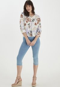Blusa a fiori con maniche a tre quarti, in tonalità di crema, marrone e viola. Abbinata a jeans cropped azzurri e sandali con zeppa.