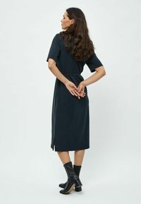 Dark blue dress with short sleeves, a fitted waist, knee-length hem, and side slit, paired with black ankle boots, featuring a textured finish.