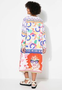 Robe longue colorée avec des motifs abstraits dans plusieurs couleurs, arborant un graphique audacieux d'une femme aux cheveux rouges et portant des lunettes de soleil au bord.