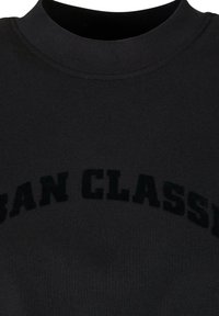 Sweat-shirt noir à col haut et lettres texturées "URBAN CLASSIC" dans une teinte plus foncée. Tissu lisse avec une coupe décontractée.
